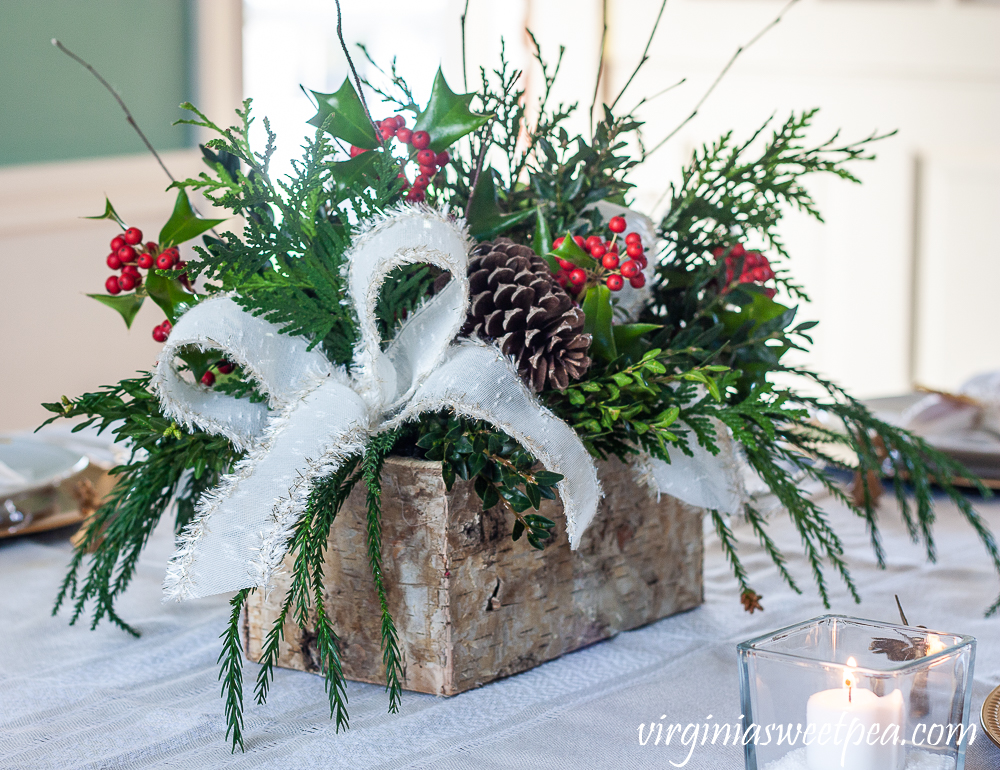 Christmas centerpiece in a Birch bark box with greenery, Holly, pinecones, twigs, and white ribbon trimmed with gold