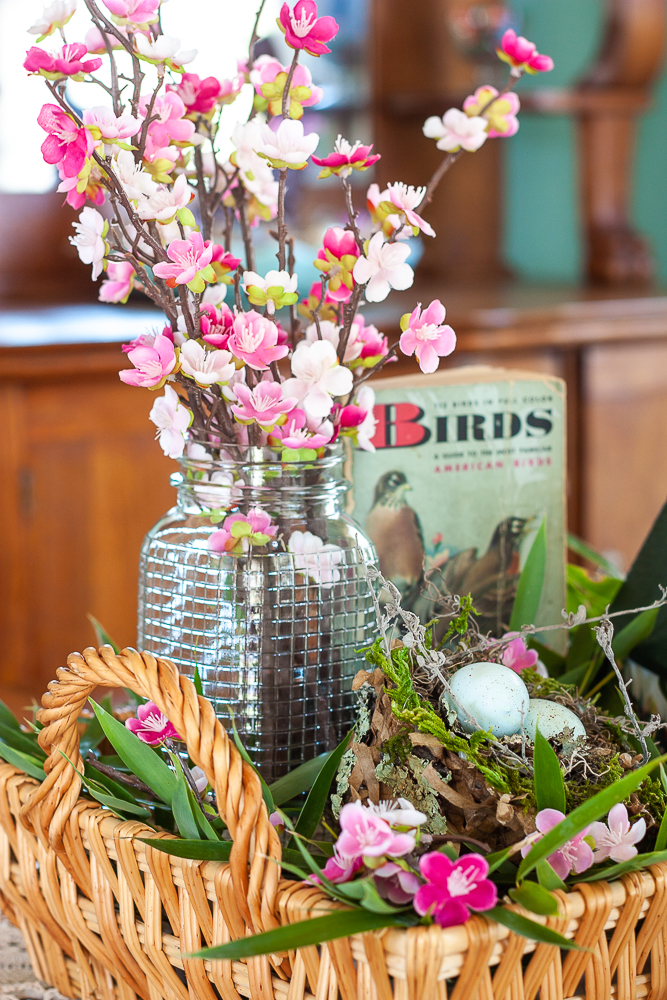 Pink faux florals in a vintage, clear, embossed Mason jar with a bird nest, and 1949 Birds A Golden Nature Guide