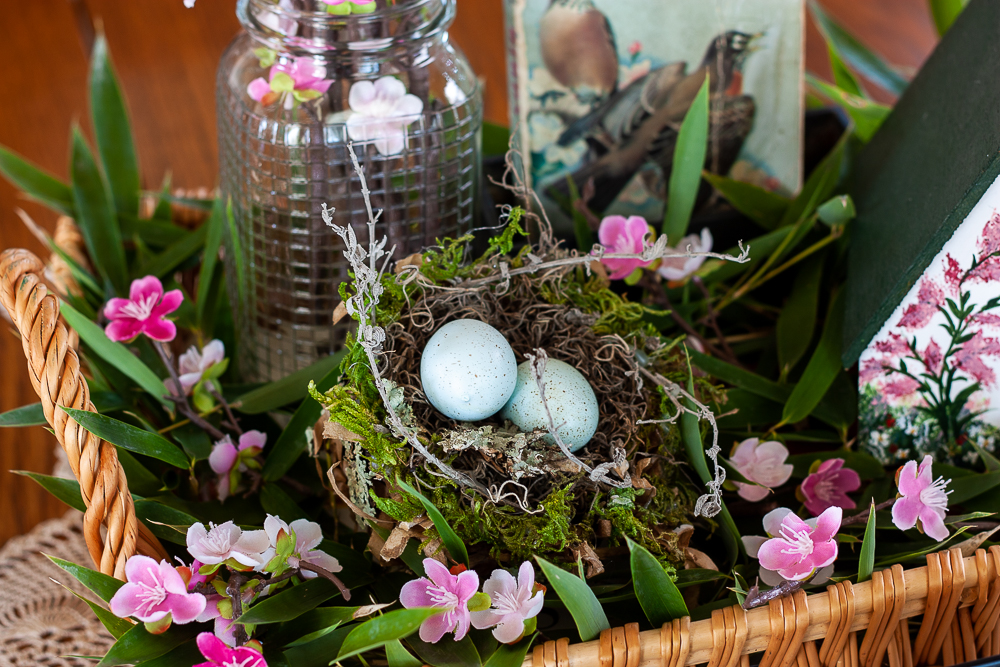 Bird themed spring centerpiece with a bird house, bird book, nest with eggs, and a Mason jar filled with pink flowers